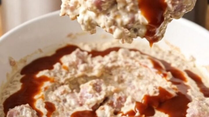 Thick crockpot BBQ sausage and bacon cream cheese dip swirled with barbecue sauce in a white bowl