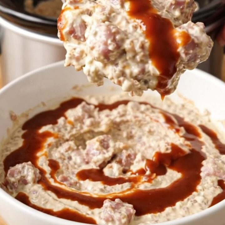 Thick crockpot BBQ sausage and bacon cream cheese dip swirled with barbecue sauce in a white bowl
