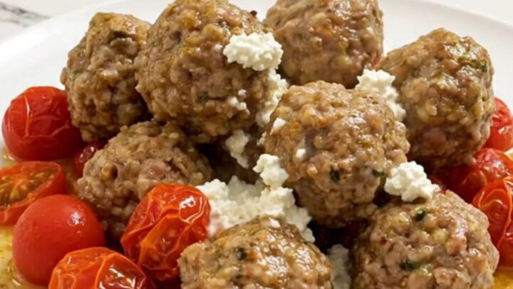 Braised Greek turkey meatballs in creamy feta sauce with burst cherry tomatoes, served on a white plate