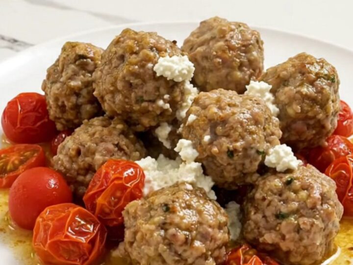 Braised Greek turkey meatballs in creamy feta sauce with burst cherry tomatoes, served on a white plate