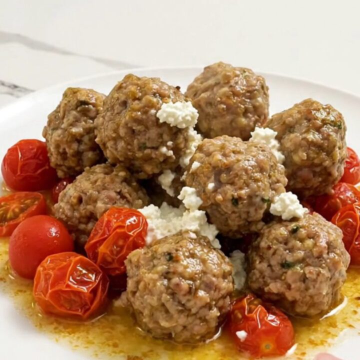 Braised Greek turkey meatballs in creamy feta sauce with burst cherry tomatoes, served on a white plate