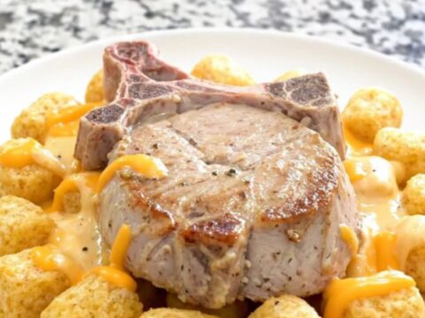Slow cooker pork chop casserole with soft potato tots and thick creamy cheddar sauce in a black ceramic insert