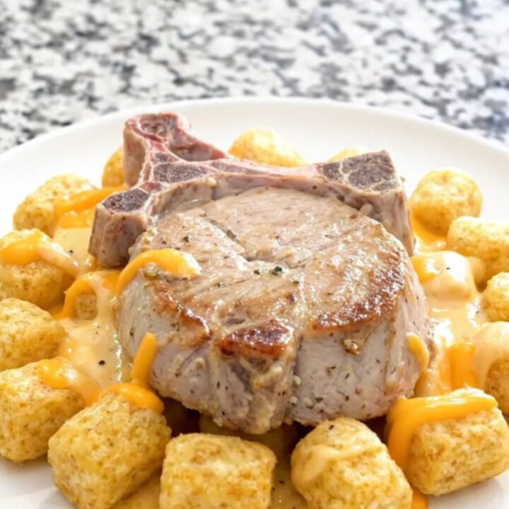 Slow cooker pork chop casserole with soft potato tots and thick creamy cheddar sauce in a black ceramic insert
