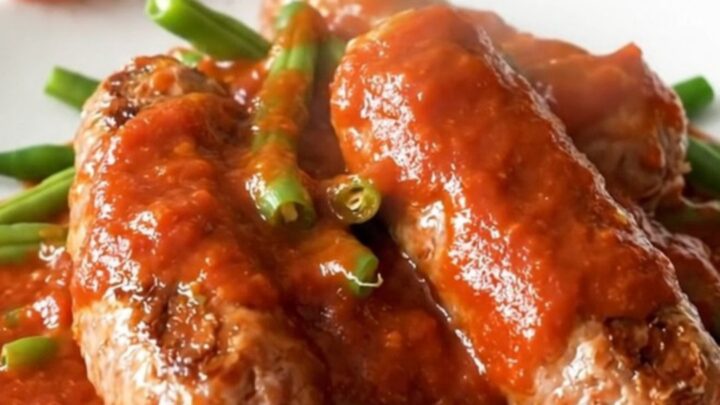 Whole Italian sausage links and green beans in thick red marinara sauce on a white plate, steam rising