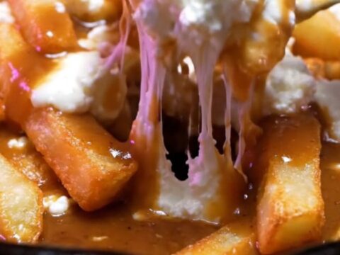 Cast-iron skillet of Montreal duck-fat poutine with glossy brown gravy pouring over fries and white cheddar curds