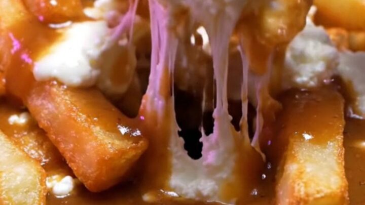 Cast-iron skillet of Montreal duck-fat poutine with glossy brown gravy pouring over fries and white cheddar curds