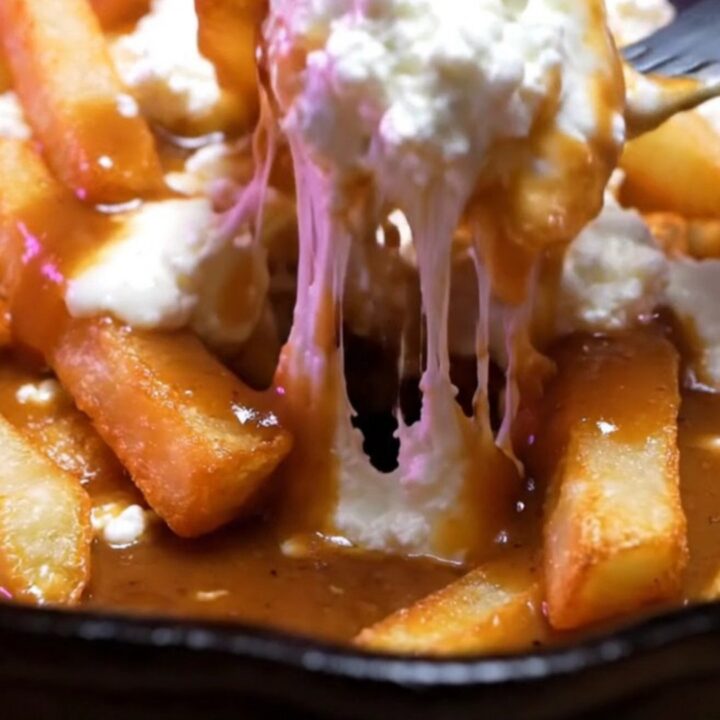 Cast-iron skillet of Montreal duck-fat poutine with glossy brown gravy pouring over fries and white cheddar curds