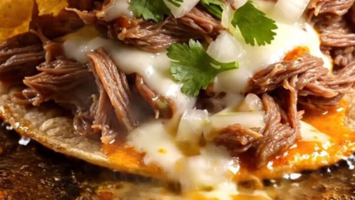 Two crispy quesabirria tacos with molten Oaxaca cheese being dipped into a bowl of glossy red beef consomé
