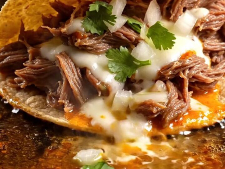 Two crispy quesabirria tacos with molten Oaxaca cheese being dipped into a bowl of glossy red beef consomé