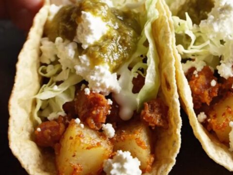 Crispy potato and chorizo taco topped with queso fresco, crema and green salsa verde on a rustic wooden board