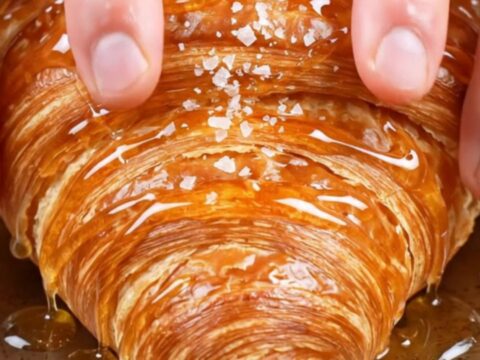 Flat smash croissant with glassy caramel crust, honey drizzle and flaky salt on a plate