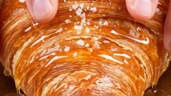 Flat smash croissant with glassy caramel crust, honey drizzle and flaky salt on a plate