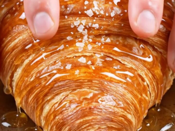 Flat smash croissant with glassy caramel crust, honey drizzle and flaky salt on a plate