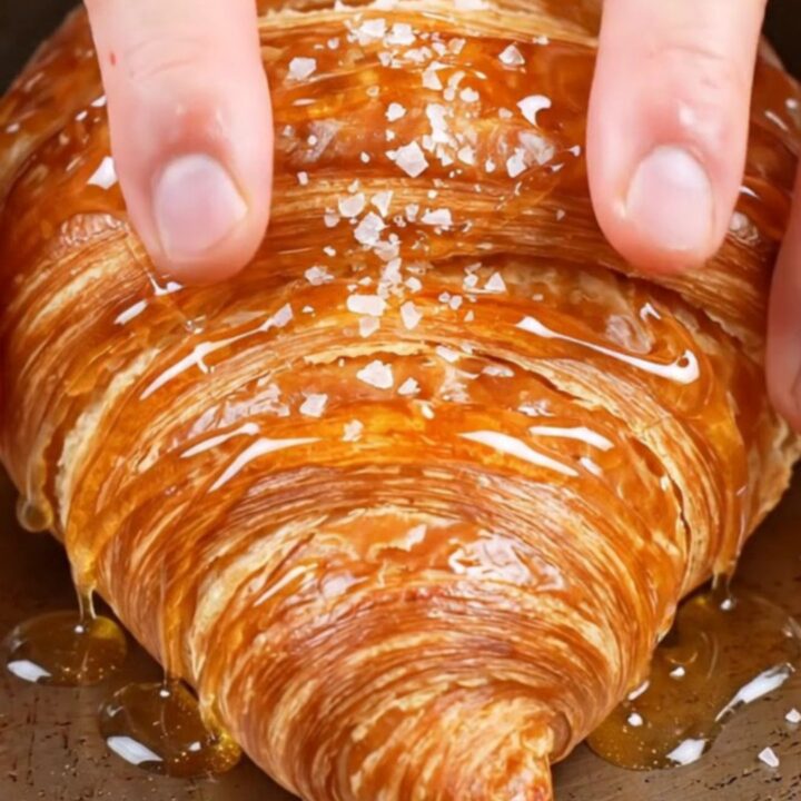 Flat smash croissant with glassy caramel crust, honey drizzle and flaky salt on a plate