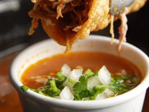 Crispy birria tacos with melted Oaxaca cheese beside a cup of red consomme topped with onion and cilantro