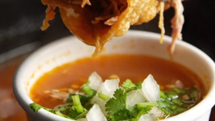 Crispy birria tacos with melted Oaxaca cheese beside a cup of red consomme topped with onion and cilantro