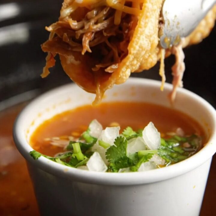 Crispy birria tacos with melted Oaxaca cheese beside a cup of red consomme topped with onion and cilantro