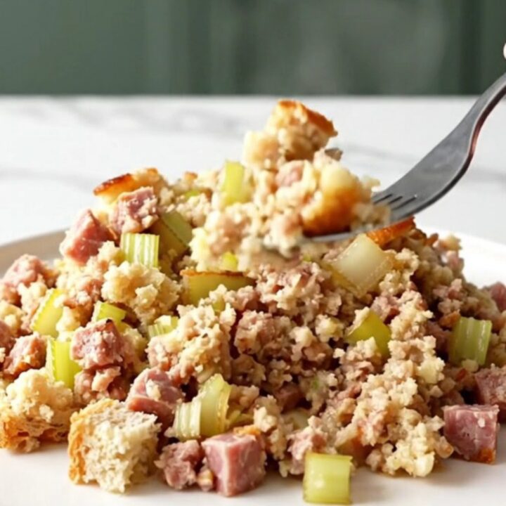 Slow cooker sausage and sage stuffing scooped onto a white plate with golden edges and browned sausage crumbles