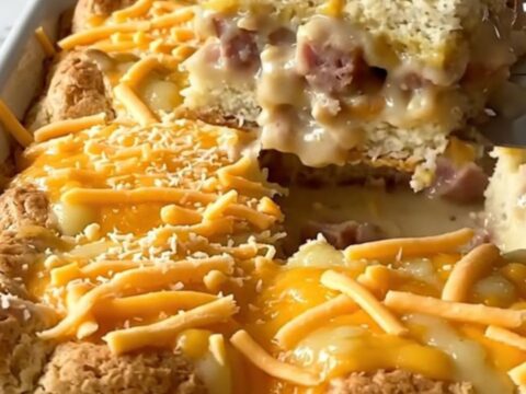Baked sausage gravy biscuit breakfast bake in a white ceramic dish, golden puffed biscuits under melted cheddar