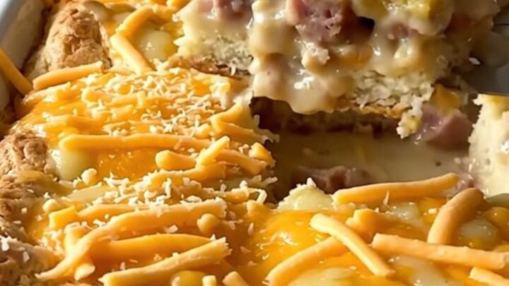 Baked sausage gravy biscuit breakfast bake in a white ceramic dish, golden puffed biscuits under melted cheddar