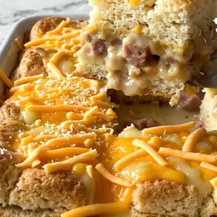 Baked sausage gravy biscuit breakfast bake in a white ceramic dish, golden puffed biscuits under melted cheddar