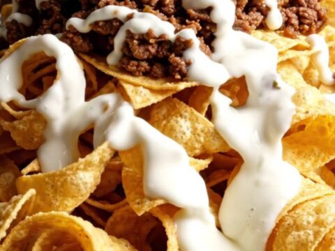 Skillet of golden spiral tortilla ribbon nachos with hot white queso cascading over crunchy curls, taco beef