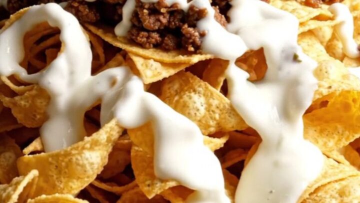 Skillet of golden spiral tortilla ribbon nachos with hot white queso cascading over crunchy curls, taco beef
