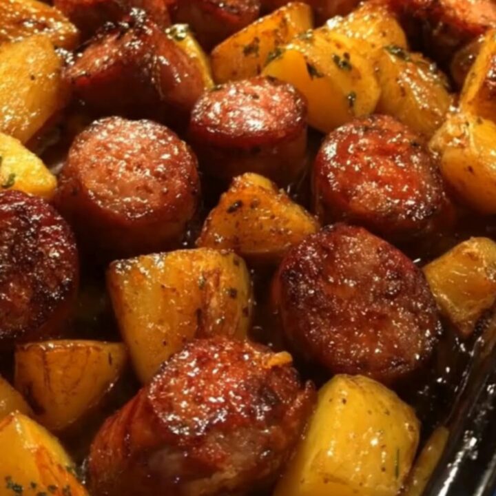 Sheet pan of honey garlic sausage bake with glazed caramelized sausage rounds, golden potato chunks, and chopped parsley