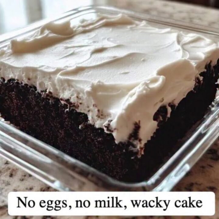 Fork cutting through white vanilla frosting into a moist dark chocolate wacky cake in a square glass dish