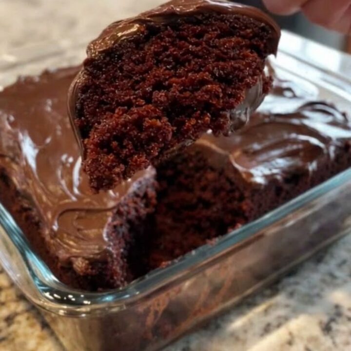 A moist slice of chocolate wacky cake with glossy frosting lifted from a glass baking dish