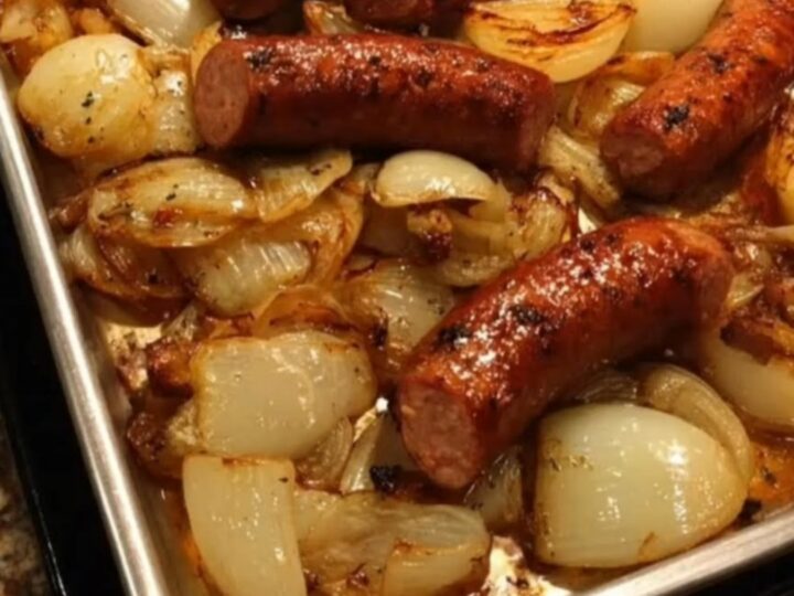Brown juicy sausages and golden caramelized onion wedges on a rimmed baking sheet, steam rising in warm kitchen light