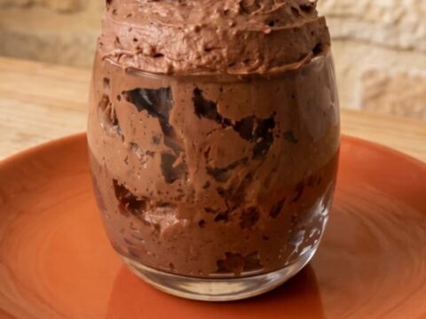 Clear glass filled with thick swirled sugar-free chocolate mousse on a terracotta plate