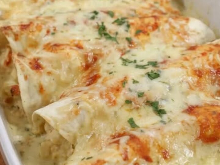 White chicken creamy enchiladas in a white baking dish with a spatula lifting one enchilada in a long stretchy cheese pull