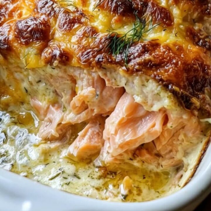Creamy baked salmon casserole in a white baking dish with a golden bubbly cheese crust and fresh dill