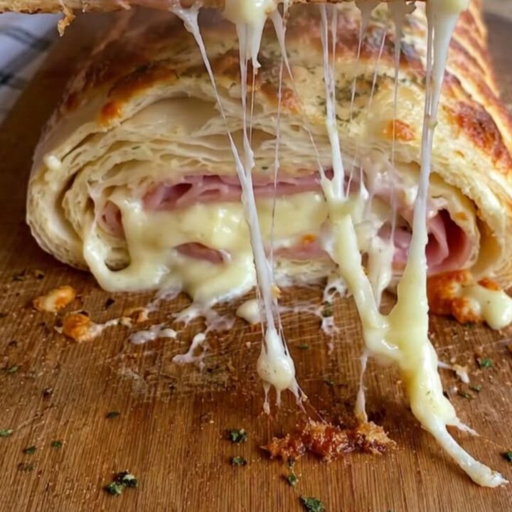 Golden baked ham and cheese stromboli on a wooden cutting board with a slice lifted in a long stretchy cheese pull