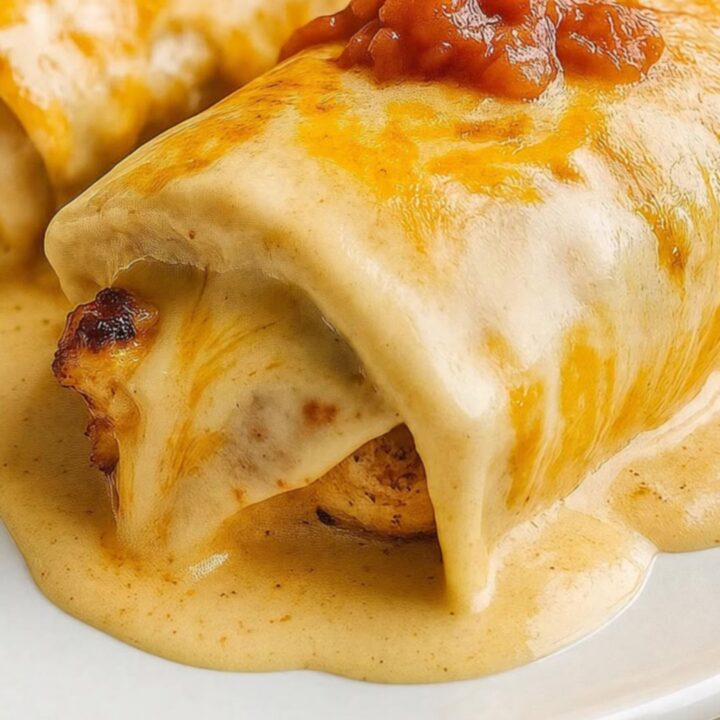 A glass baking dish of bubbly cheesy chicken enchiladas in glossy cream sauce, a spatula lifting one with a long cheese pull