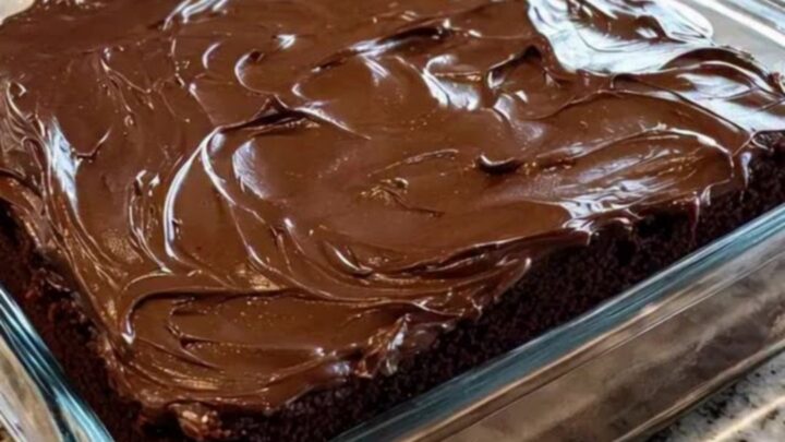 Slice of moist chocolate wacky cake with swirled chocolate frosting on a white plate