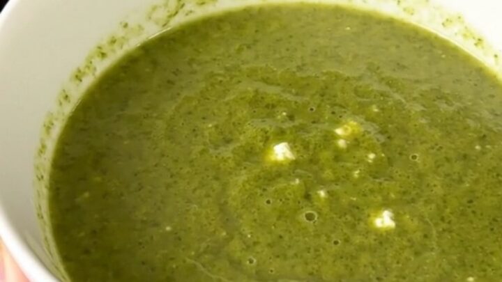 Silky pale green zucchini and goat cheese soup steaming in a white bowl on a kitchen counter