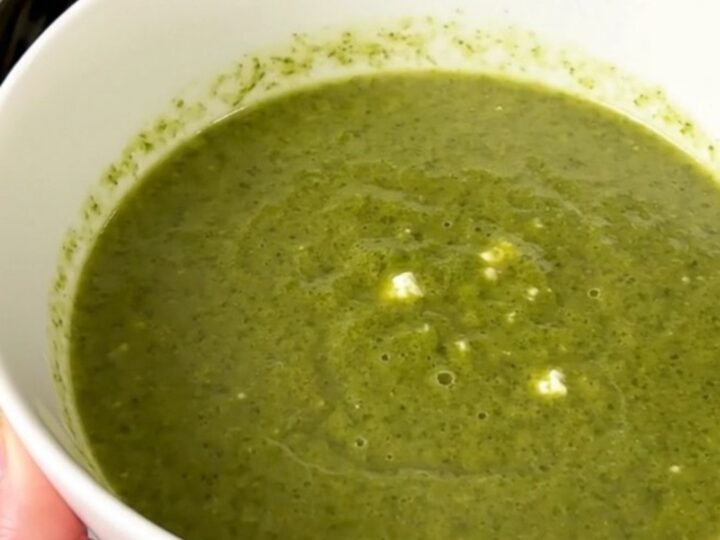 Silky pale green zucchini and goat cheese soup steaming in a white bowl on a kitchen counter