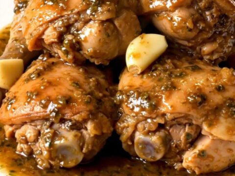 Slow-cooked garlic chicken thighs in thick herb sauce with soft garlic cloves on a white plate