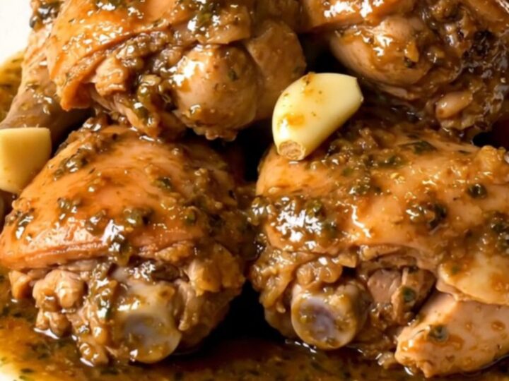 Slow-cooked garlic chicken thighs in thick herb sauce with soft garlic cloves on a white plate