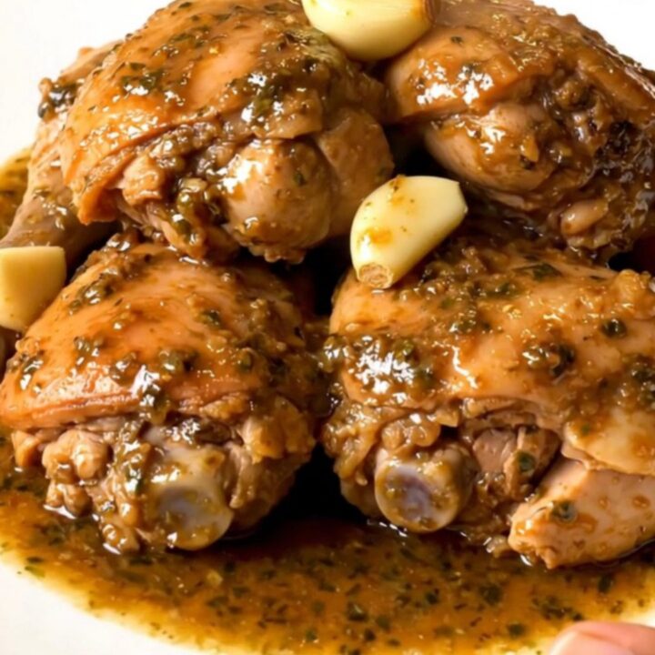 Slow-cooked garlic chicken thighs in thick herb sauce with soft garlic cloves on a white plate