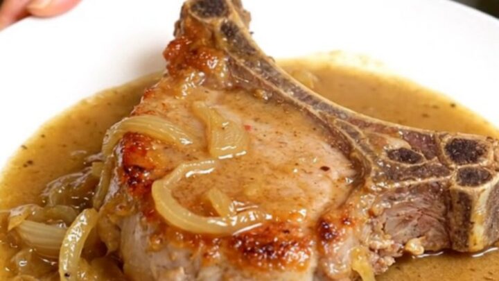 Slow cooker creamy onion pork chops smothered in thick onion gravy on a white plate with tender onions