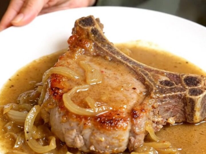 Slow cooker creamy onion pork chops smothered in thick onion gravy on a white plate with tender onions