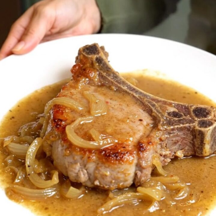 Slow cooker creamy onion pork chops smothered in thick onion gravy on a white plate with tender onions