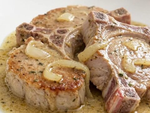 Slow cooker pork chops in creamy white wine sauce with soft onions, served on a white plate with steam rising