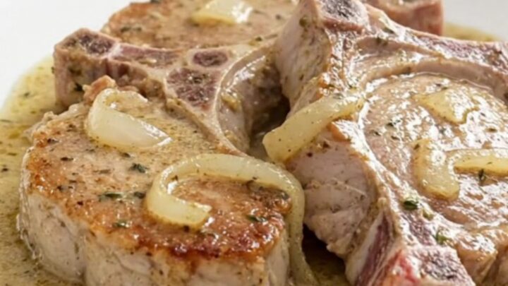 Slow cooker pork chops in creamy white wine sauce with soft onions, served on a white plate with steam rising