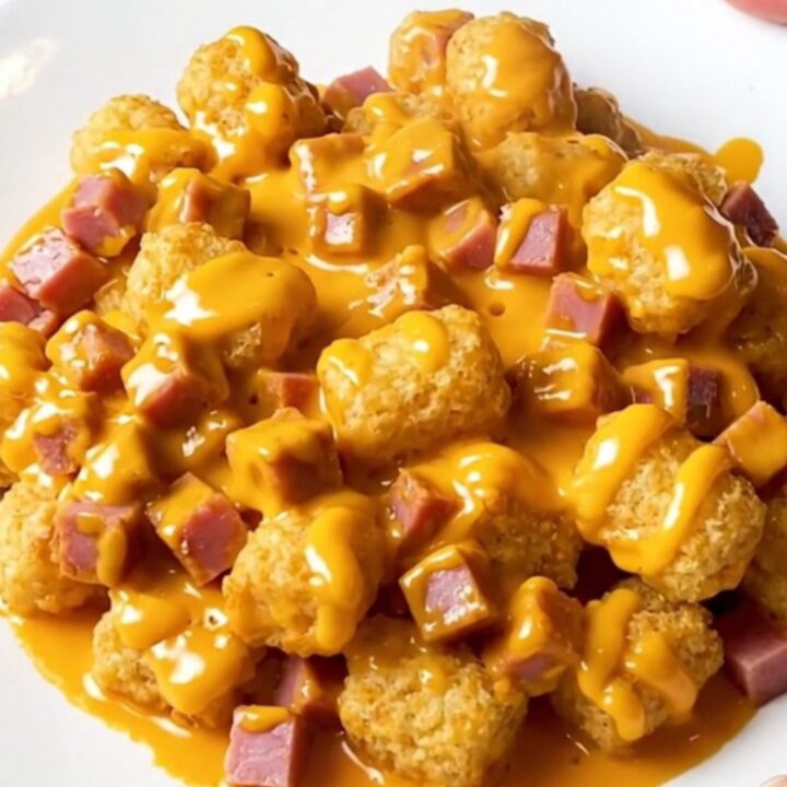 Slow cooker ham and potato tot casserole with melted cheddar sauce in a cream stoneware crock on a beige countertop