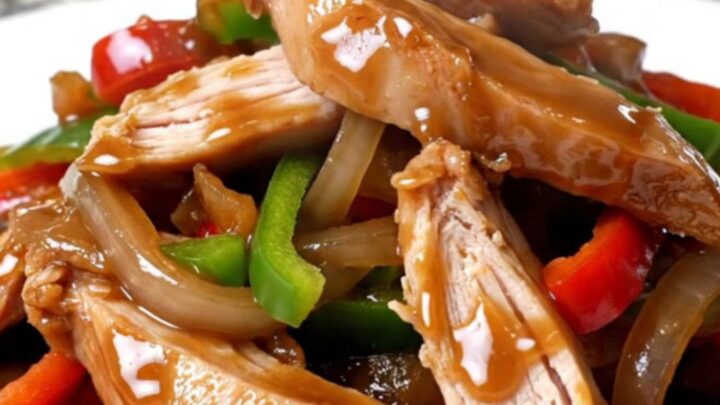Crockpot turkey pepper steak strips with peppers and onions coated in thick brown sauce on a white plate