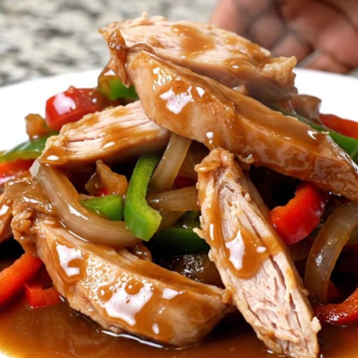 Crockpot turkey pepper steak strips with peppers and onions coated in thick brown sauce on a white plate